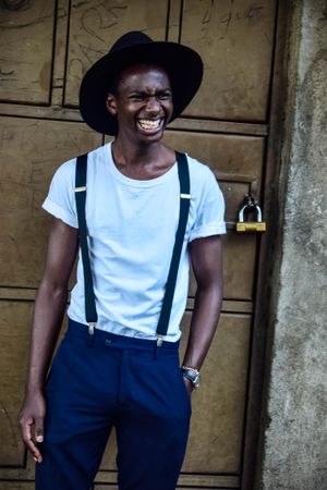 Portrait of man wearing fedora hat smiling and standing beside a door