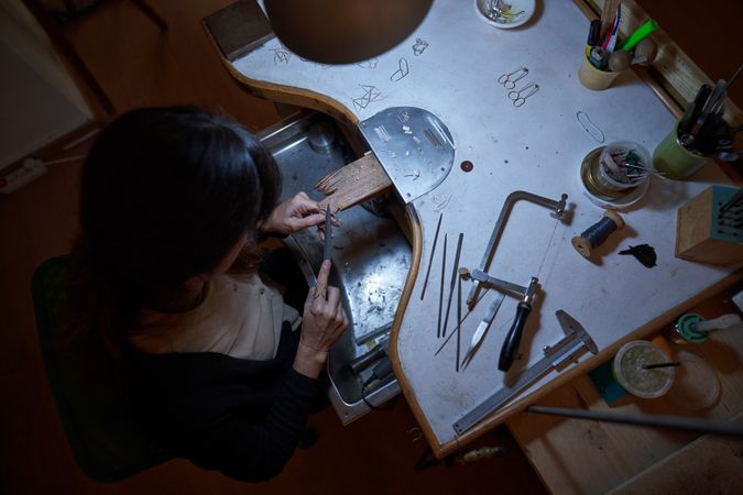 Anonymous female jeweler working with needle file at workbench