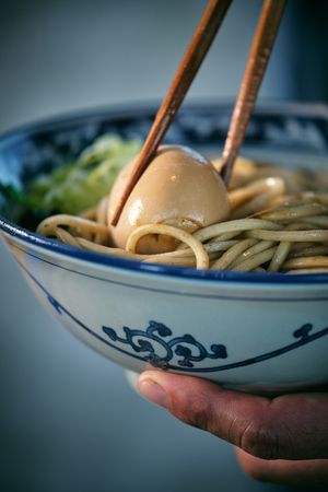 Crop person with boiled egg between chopsticks in ramen
