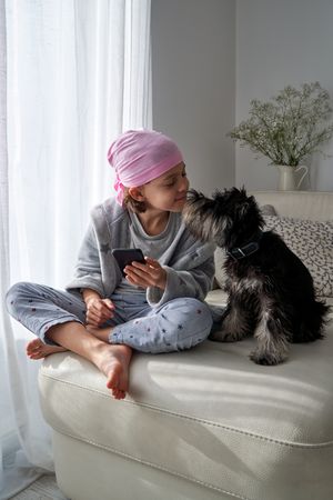 Kid in bandana with cellphone caressing dog on couch