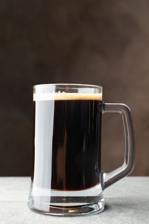Glass of dark beer on grey table, space for text