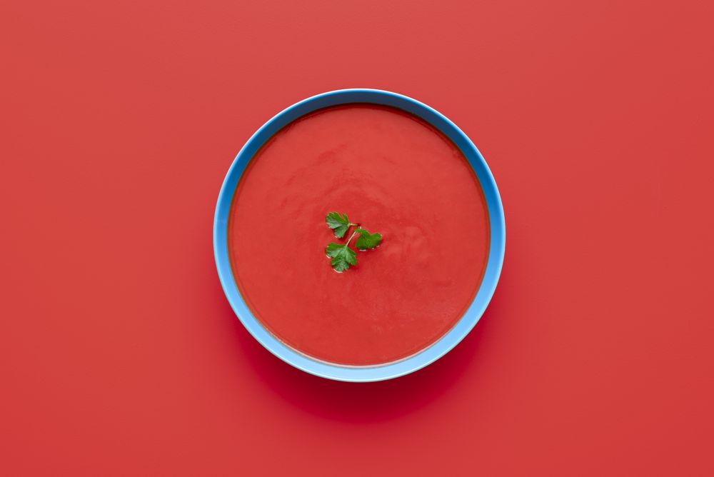 Tomato cream soup bowl, above view on a red background