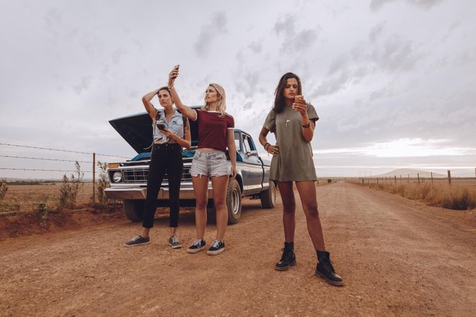 Female friends checking phone reception after car breaks down on quiet road
