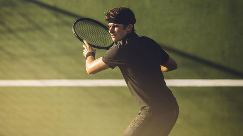Young player playing tennis on hard court