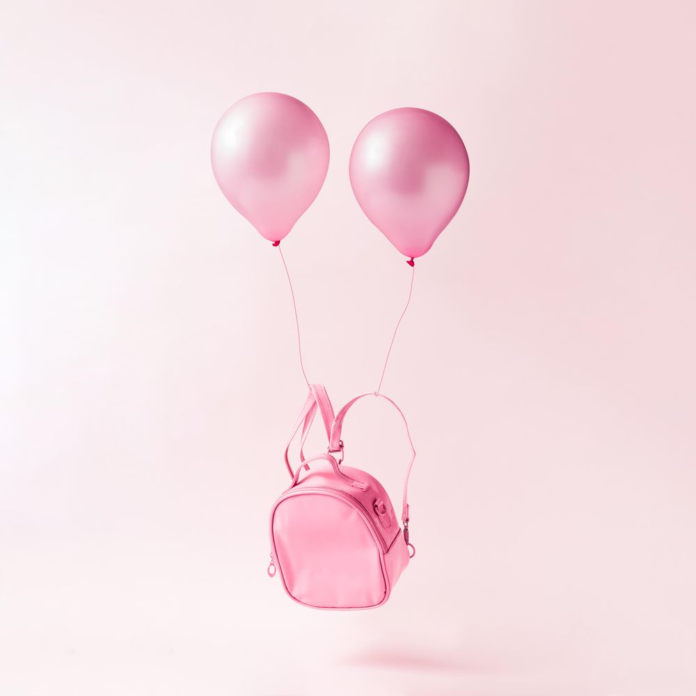 Pastel pink backpack bag with balloons floating on pink background