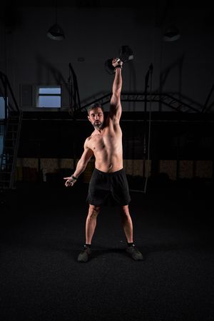 Sporty guy lifting dumbbell in dark fitness center
