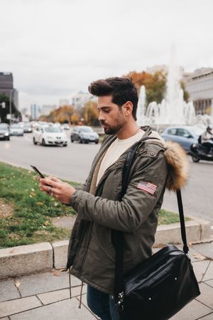 Young male in warm jacket using smartphone