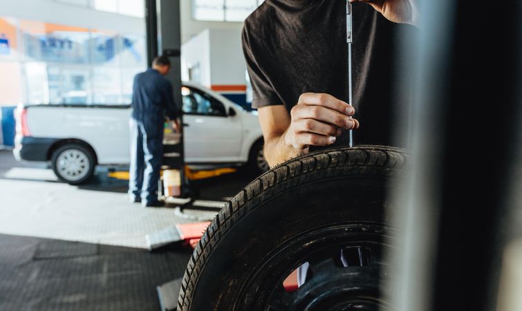 Mechanic checking car tire tread depth with caliber