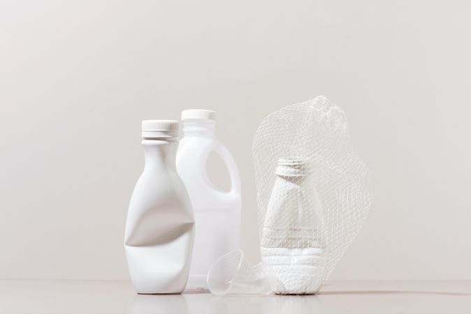 Three crushed plastic bottles and cup on neutral background