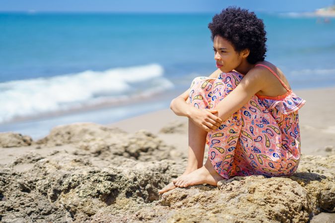 Woman sitting on the rocks on the coast looking out to the sea with head down to knees