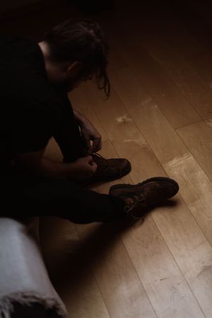 Male traveler in casual wear tying shoelaces at home