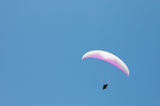 Skydiver with a pink parachute flies across the blue sky