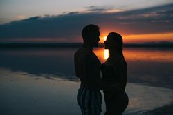 Couple hugging on beach of lake at sunset