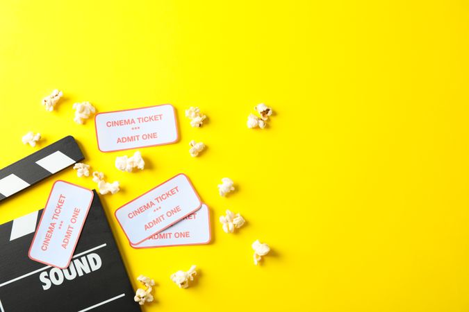 Flat lay composition with clapperboard, popcorn and tickets on yellow background