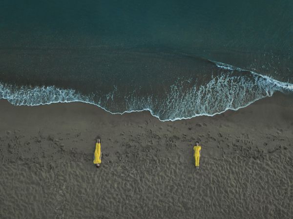 Top view of two people in yellow outfits laying on beach in Provincia di Salerno, Campania, Italy