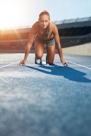 Young woman sprinter in the starter position on a race track at a sports stadium
