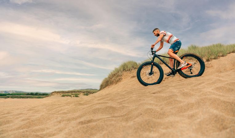 Male riding bicycle down sandy dune with copy space