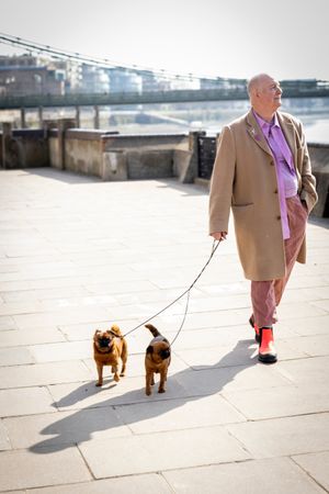 Man walking by river with two dogs, vertical