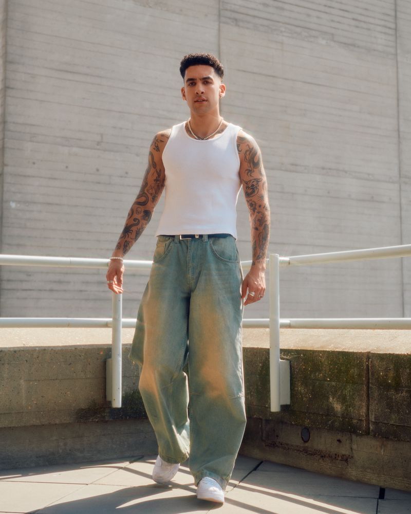 Man in vest and jeans walking towards camera among concrete structures