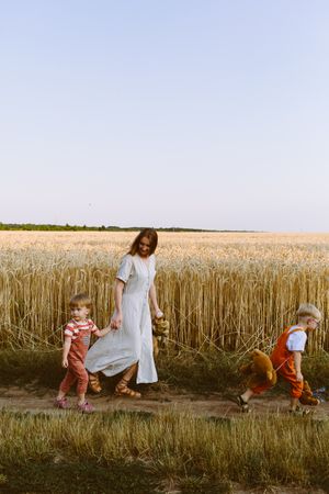 Young mother with little sons walking near wheat field in countryside