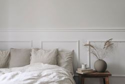 Bedside table with books and vase next to comfortable bed
