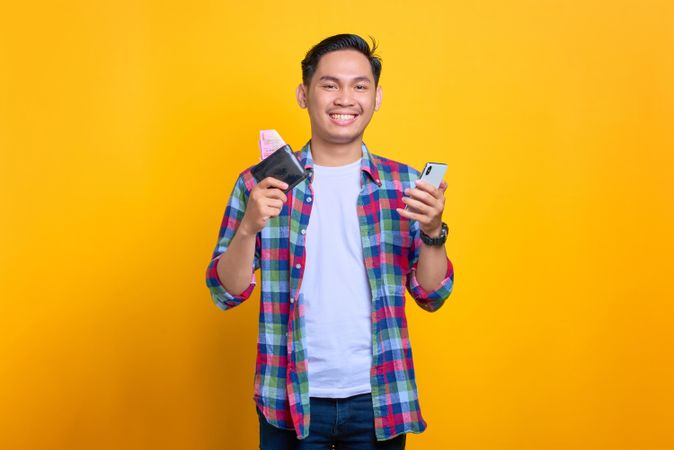 Content Asian man smiling while holding wallet and his phone
