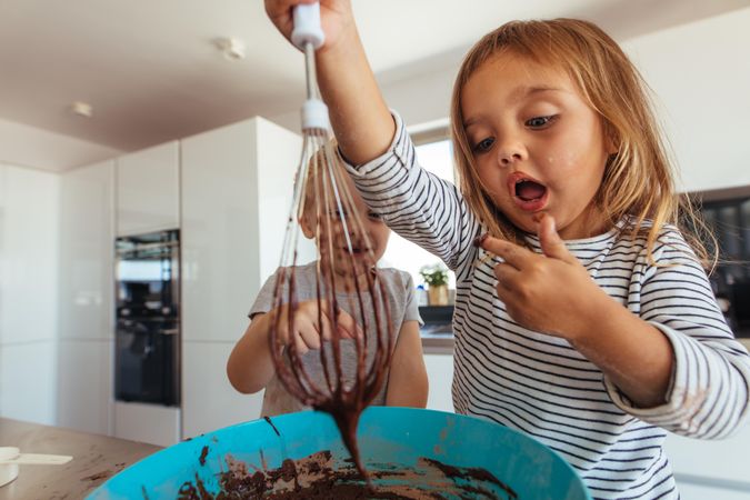 Young girl licking batter from bowl in the kitchen