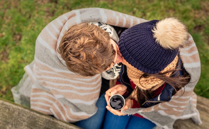 Top view of couple kissing while holding warm coffee on park bench