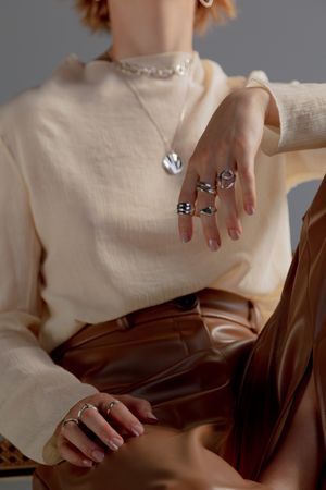 Cropped image of woman in beige top and brown leather pant wearing rings