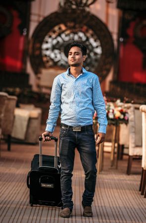 Young man in blue dress shirt walking with luggage in a venue