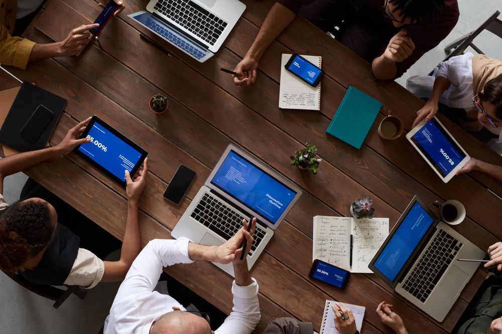 Team Collaborating Around Wooden Table with Laptops and Tablets in Office