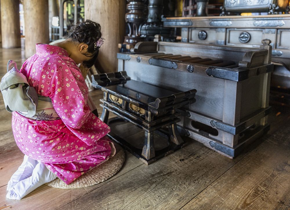 Back view of young woman in kimono praying at the altar