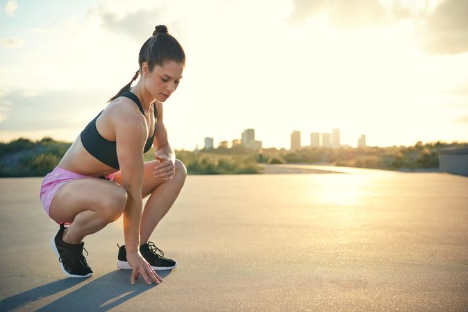 Muscular woman crouching down touching cement  between workouts
