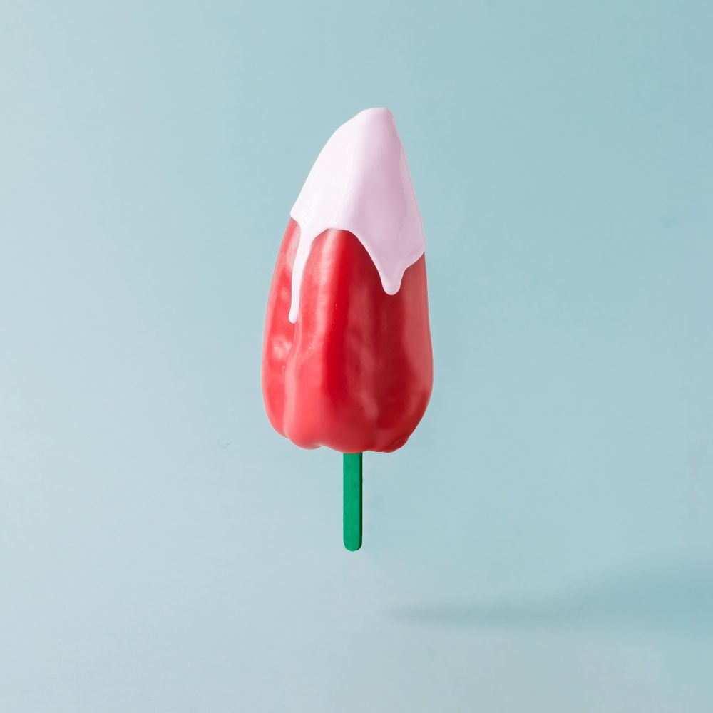 Red pepper with ice cream stick topped with pink syrup on pastel blue background