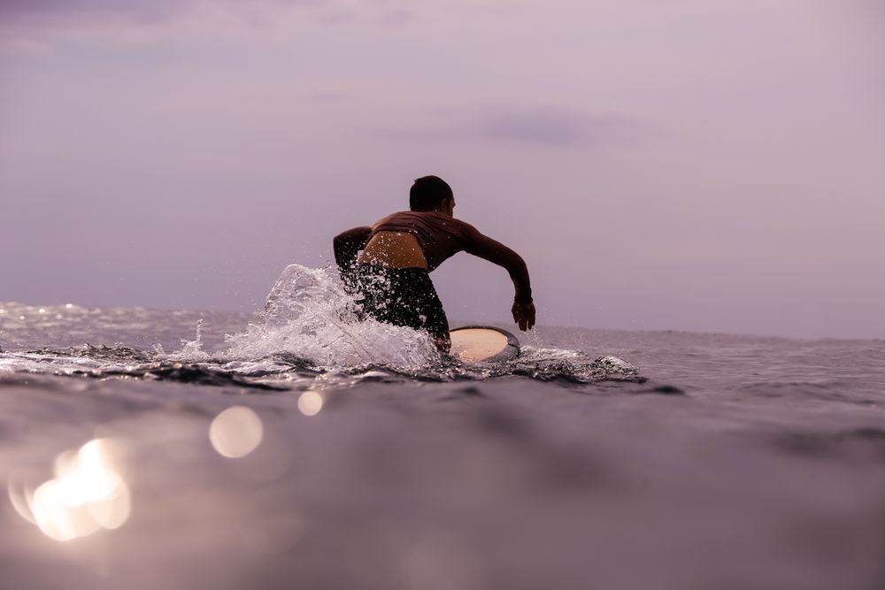 Man on surf board floating on water and cloudy sky