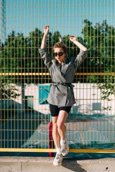 Stylish woman in sunglasses raising hands and leaning on lattice