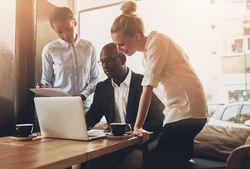 Multi-ethnic group gathered around a laptop and working