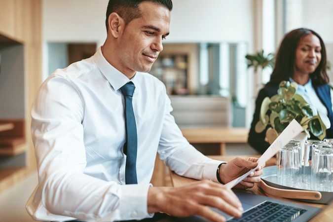 Man holding paper and typing at a laptop