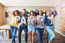 Multi-ethnic friends standing in a line holding silver balloons that say “party”