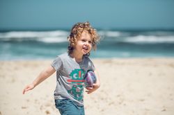 Cheerful boy with ball walking on beach