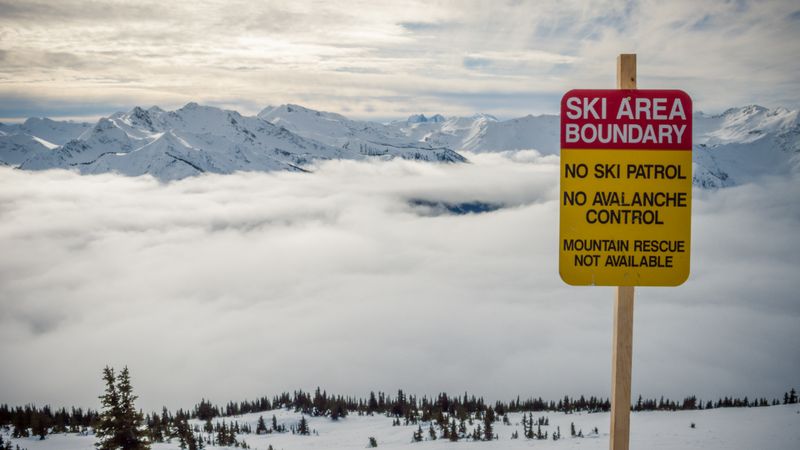 Sign with ski area boundary title on hill with snow and clouds between mountains