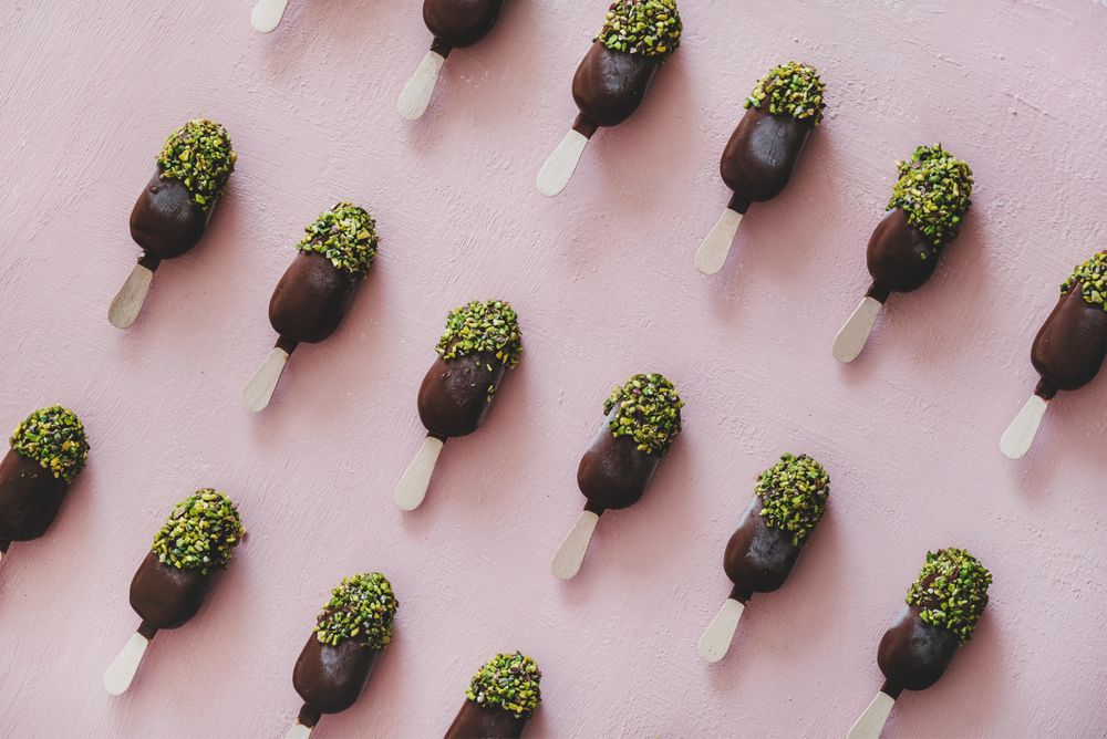Diagonal rows of ice cream chocolate pistachio popsicles, pink background