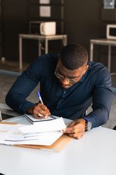 Black male writing in notepad near laptop in office