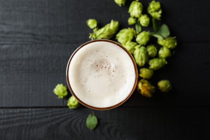Glass of beer and hop cones on wooden background, top view