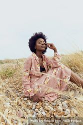 Woman in pink floral dress sitting on brown grass field 56EQY0