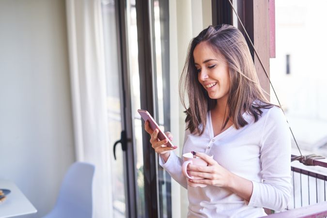 Smiling woman with smartphone eating at table at home