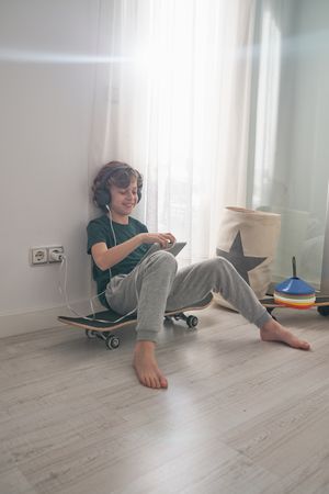 Positive preteen skater watching video on tablet in room