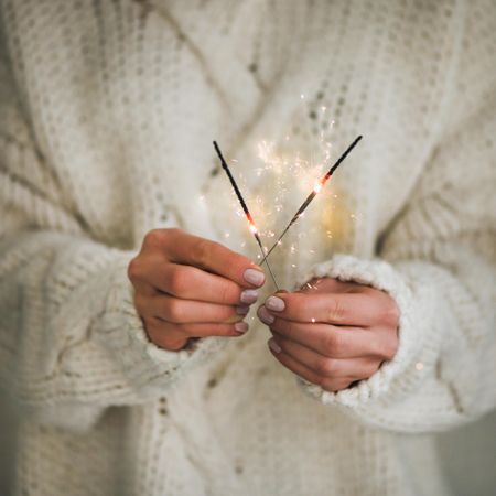 Woman holding two sparklers,  sweater, square crop