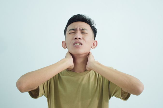 Asian young man touching neck in pain in studio shoot