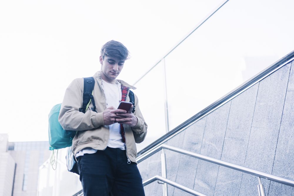 Man walking down stairs with backpack while using mobile outdoors